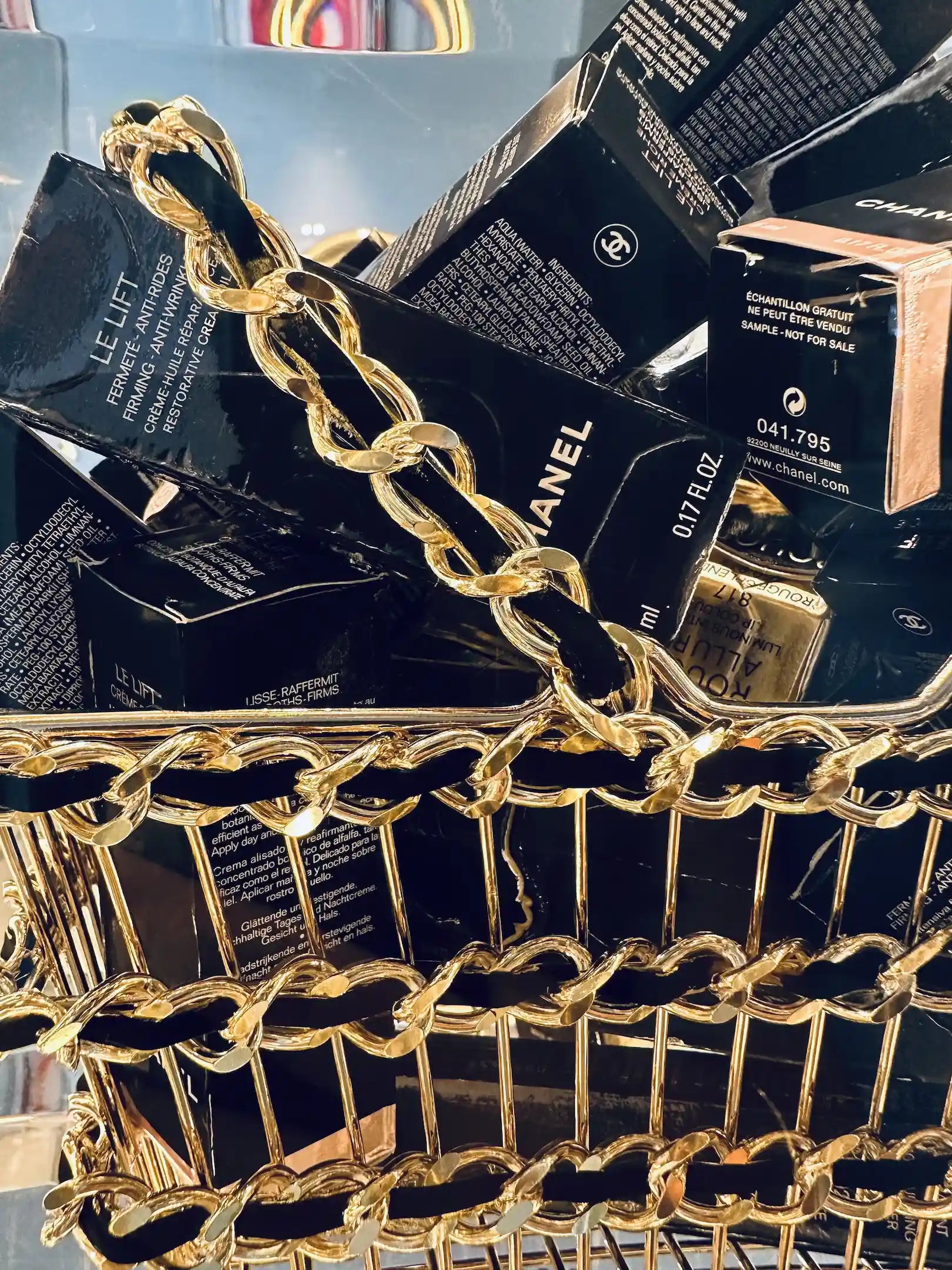 Un Basket bag avec des anses en chaîne dorée déborde de boîtes de cosmétiques Chanel noires, préparant le terrain pour "Chanel overdose" de Fred Allard.