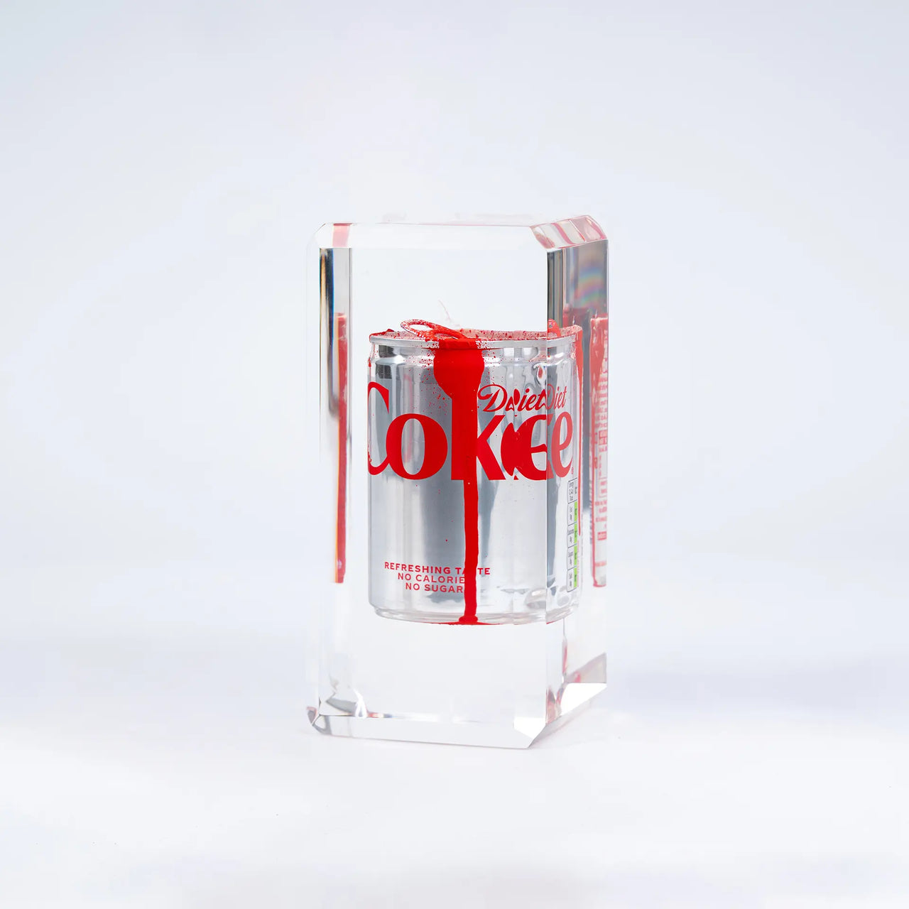 Le Drop #3 Coca-Cola de Fred Allard représente une canette de Diet Coke argentée partiellement recouverte de peinture rouge, enfermée dans un bloc rectangulaire transparent et présentée sur un fond blanc uni.