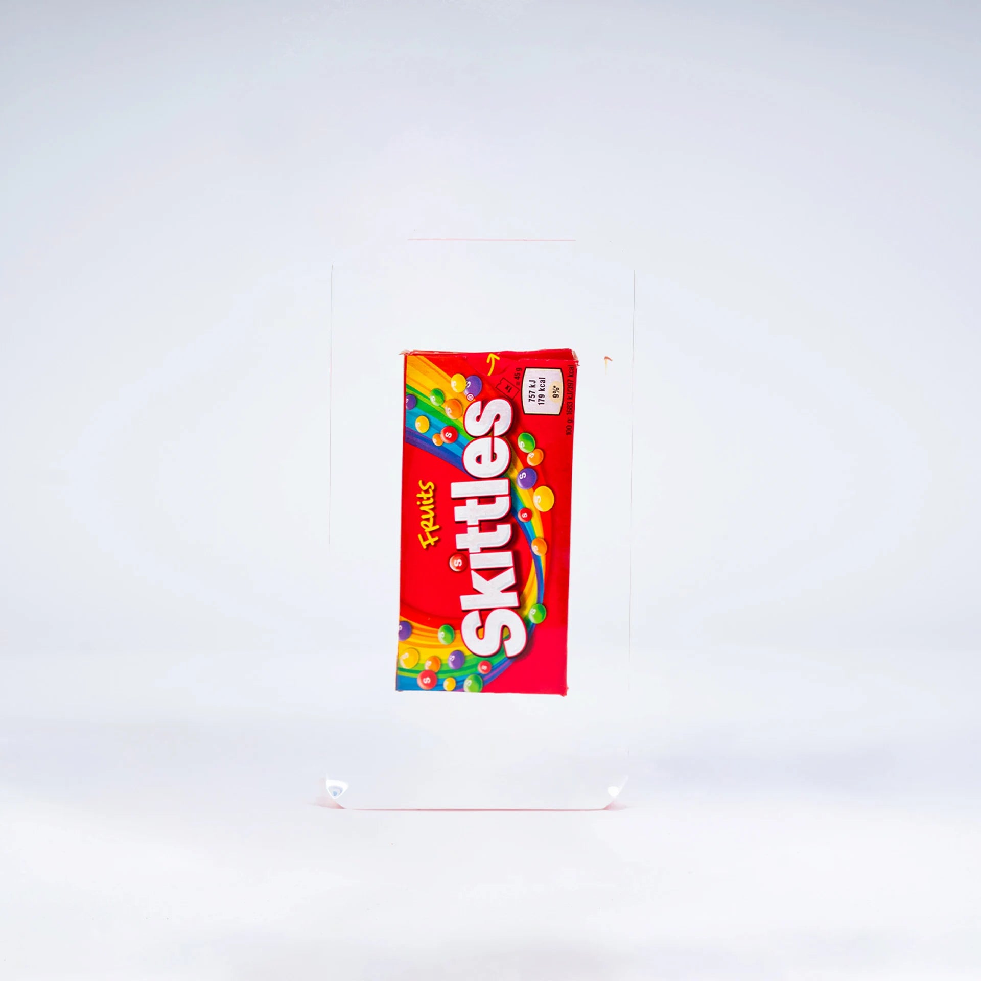 Un paquet de Skittles Fred Allard rouge se détache sur un fond blanc uni.