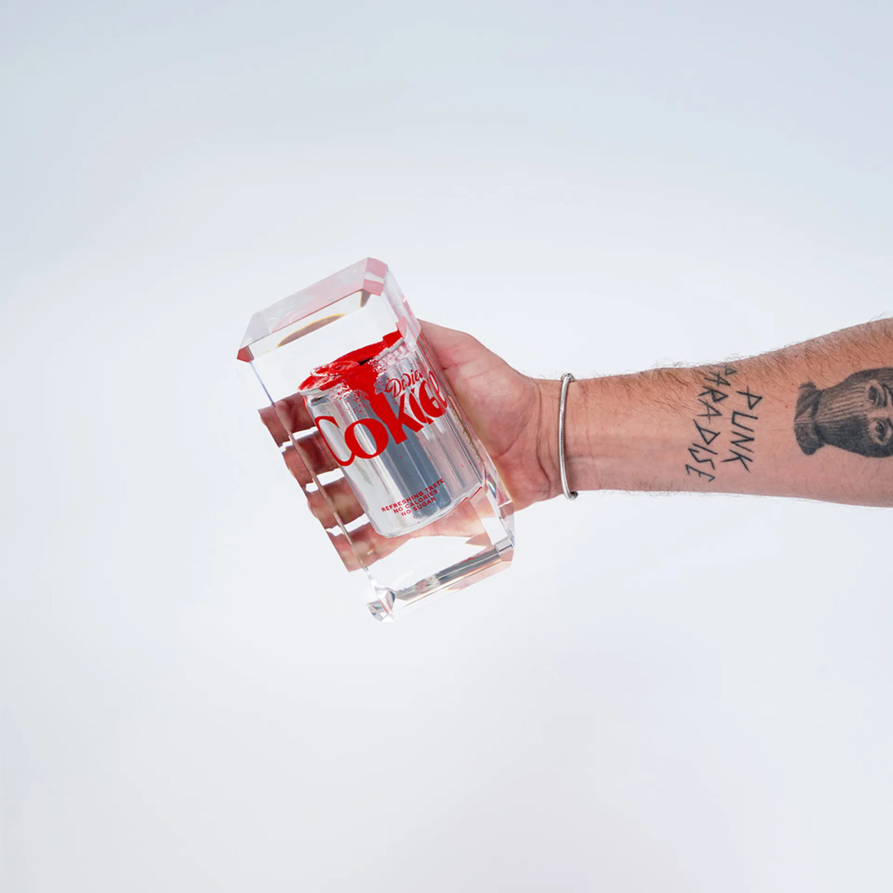 Le Drop #3 Coca-Cola de Fred Allard représente une canette de Diet Coke argentée partiellement recouverte de peinture rouge, enfermée dans un bloc rectangulaire transparent et présentée sur un fond blanc uni.